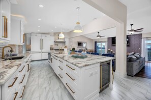 Une cuisine spacieuse avec des meubles blancs, un plan de travail en marbre et un grand îlot central.