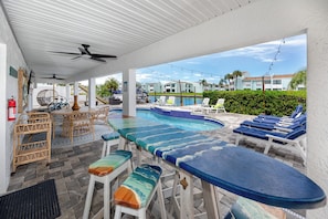 An outdoor pool area with lounge chairs, a table, and a ceiling fan. - Luxury Waterfront Heated Pool Dock Golf Cart (Indian Rocks Beach)