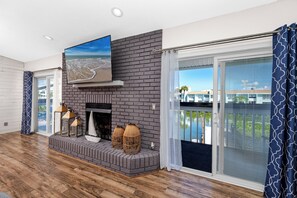 A living room with a fireplace, a large TV mounted on the wall, and a view of a pool through the sliding glass doors. - Luxury Waterfront Heated Pool Dock Golf Cart (Indian Rocks Beach)