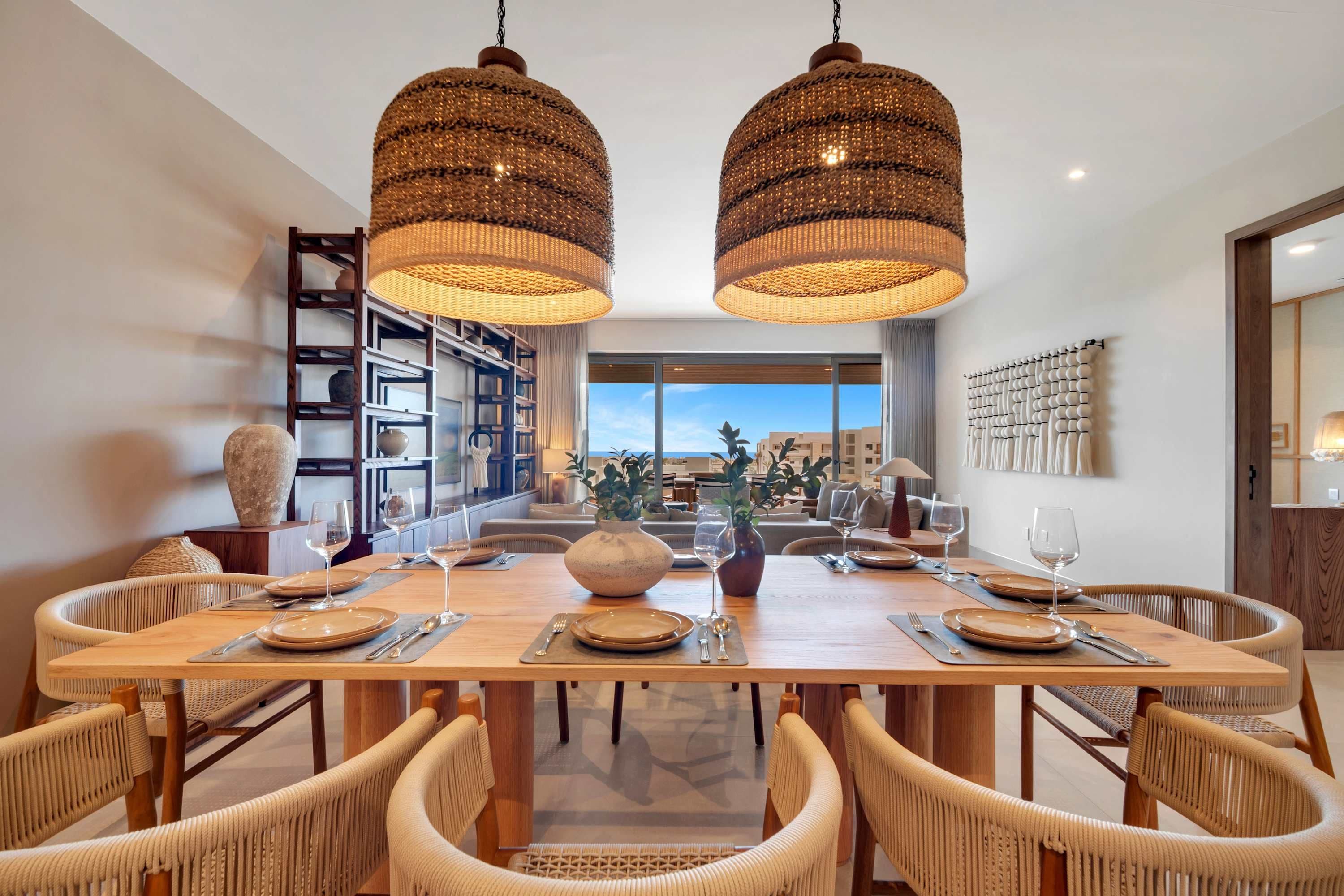 A dining area with a large wooden table, wicker chairs, and two hanging rattan chandeliers.