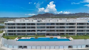 Ein mehrstöckiges Hotel mit Schwimmbad, mehreren Balkonen und Blick auf Berge.
