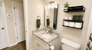 A bathroom with a white sink, a mirror, a toilet, and shelves with towels and toiletries. - Modern 2BR - King Bed - Pet-Friendly - Sleeps 6 (Boiling Springs)