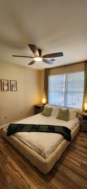 A bedroom with a bed, a ceiling fan, a window with blinds, and two bedside lamps. - Modern 2BR - King Bed - Pet-Friendly - Sleeps 6 (Boiling Springs)