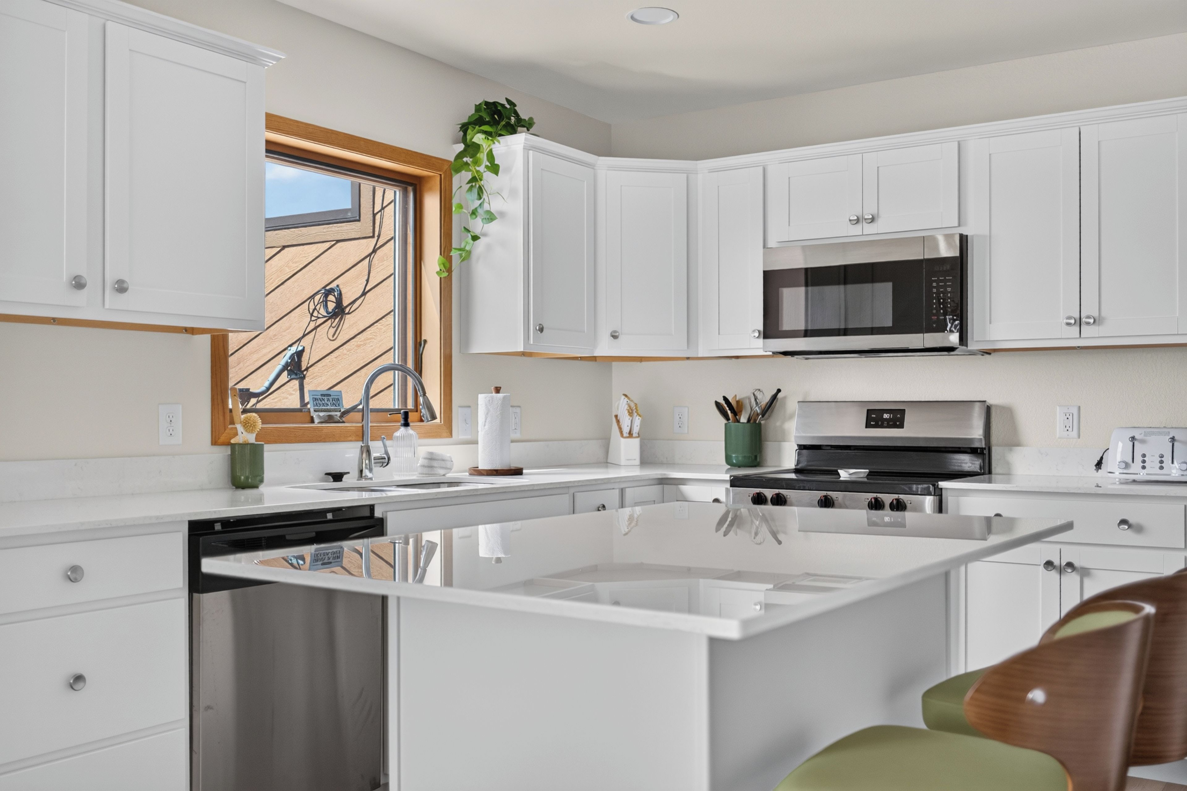 Une cuisine moderne avec des meubles blancs, un îlot central, des appareils électroménagers en acier inoxydable et une fenêtre offrant une belle vue.