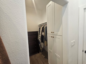 A narrow hallway with a closet containing hanging clothes and a dark dresser. - Vaulted 12 ft ceilings studio gated with  private bathroom, W/D, walk in closet. (Los Angeles)