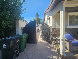 A gated driveway leading to a house with a stone wall and a wicker chair outside. - Vaulted 12 ft ceilings studio gated with  private bathroom, W/D, walk in closet. (Los Angeles)