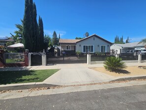 A residential house with a gated driveway, a lawn, and a palm tree. - Vaulted 12 ft ceilings studio gated with  private bathroom, W/D, walk in closet. (Los Angeles)