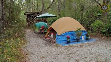 Un terrain de camping avec des tentes, une table, des chaises et une petite construction.