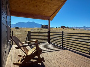 A wooden deck with a rocking chair, a metal fence, and a view of mountains and houses. - CGOs Lookout A spacious 2-bedroom 2 king beds 2 bath house in Emigrant (Emigrant)