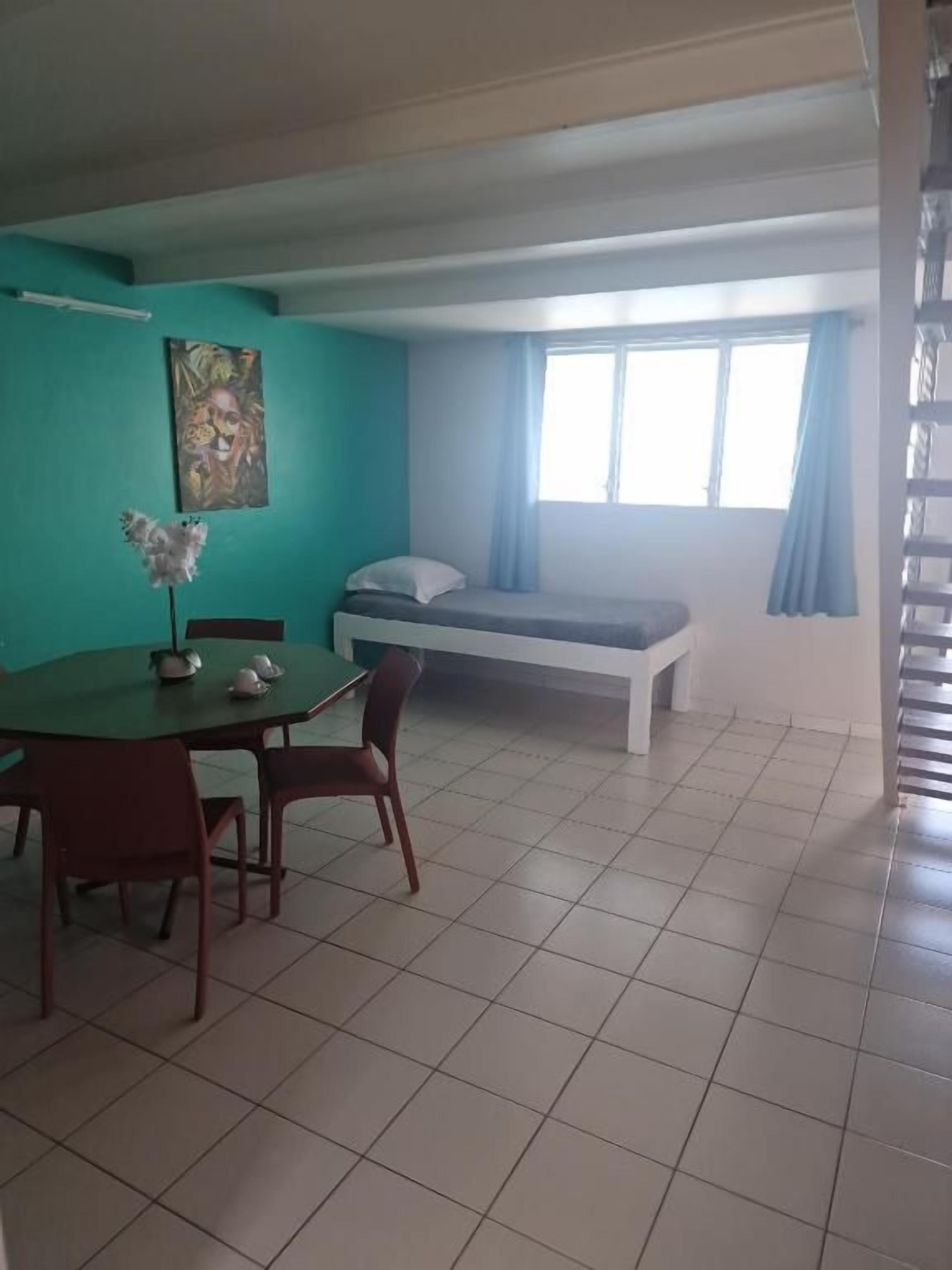 A room with a bed, a dining table with chairs, a window with curtains, and a painting on the wall.