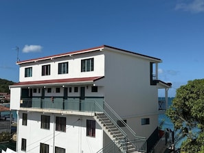 Un edificio de dos pisos con techo rojo, un balcón en el nivel superior y una escalera que conduce hacia arriba.