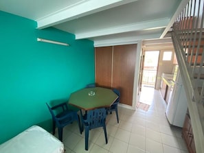 Una habitación con paredes color turquesa, una mesa de madera con sillas azules, una cama y una escalera que lleva a otra zona.