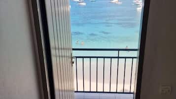 A view from a balcony to a beach with boats and a clear sky.