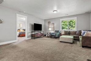 A living room with a flat-screen TV, a coffee table, a sofa, and a window with a view of trees. - Delightful, walkable 4-bedroom family home (Coeur d'Alene)