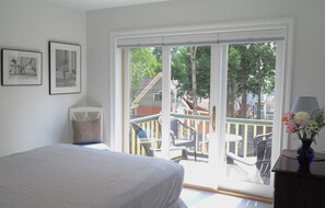 Ein Schlafzimmer mit einem Bett, einem Fenster mit Blick auf einen Balkon und zwei gerahmten Bildern an der Wand.