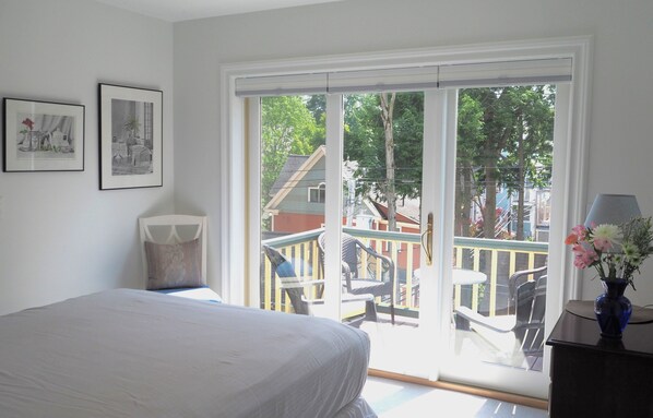 A bedroom with a bed, a window with a view of a balcony, and two framed pictures on the wall.