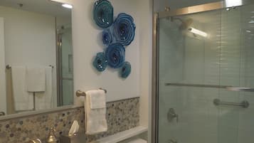 Een badkamer met een glazen douchecabine, een wastafel met kraan, een spiegel en decoratieve wanddecoratie.