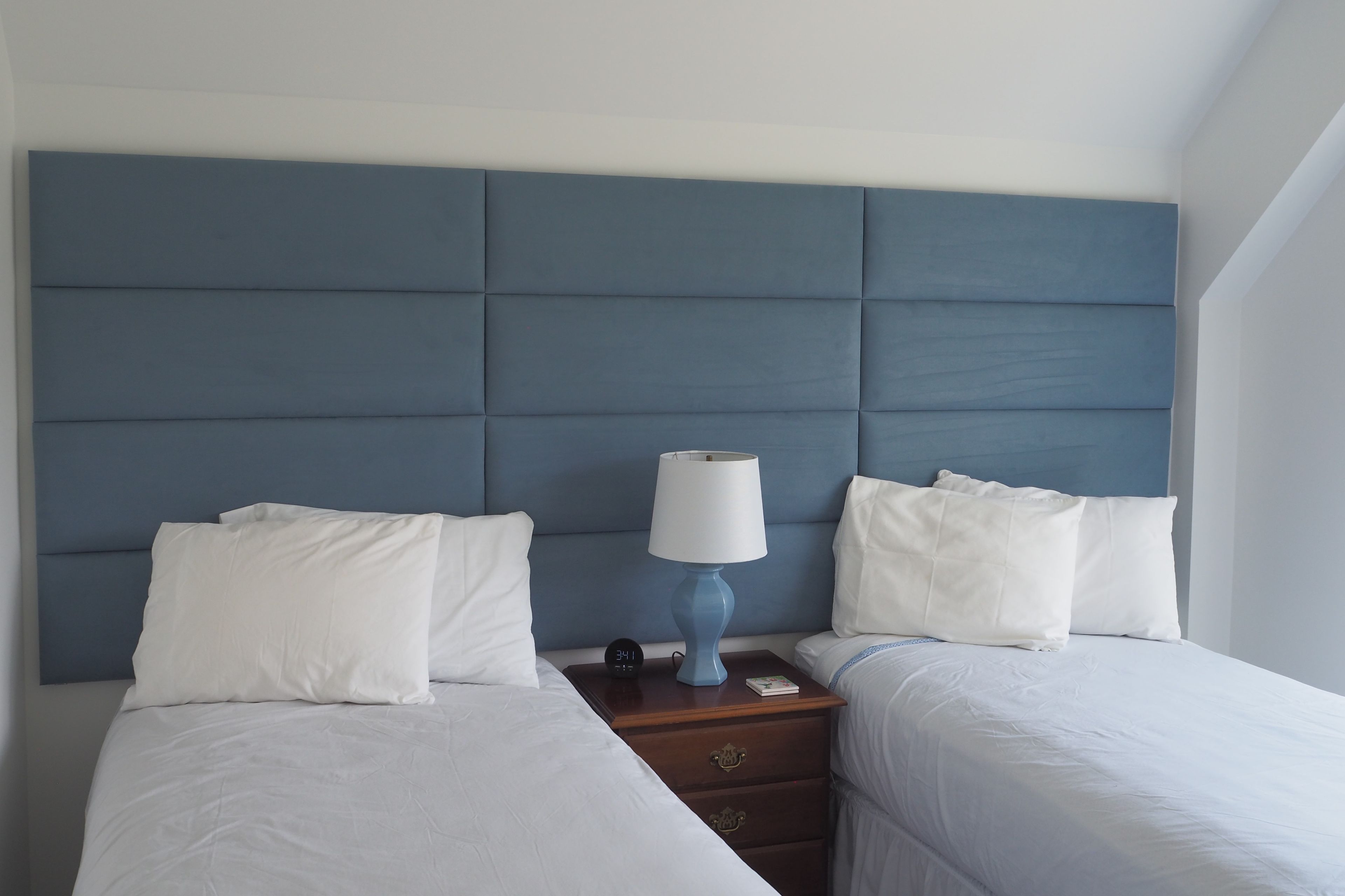 A hotel room with two single beds, a nightstand with a lamp, and a digital clock.