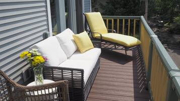 Una terraza de madera con un sofá blanco y dos sillas amarillas, una silla de mimbre y un jarrón con flores.