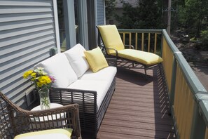 Eine Holzterrasse mit einer weißen Couch und zwei gelben Stühlen, einem Korbsessel und einem Blumenvasen.