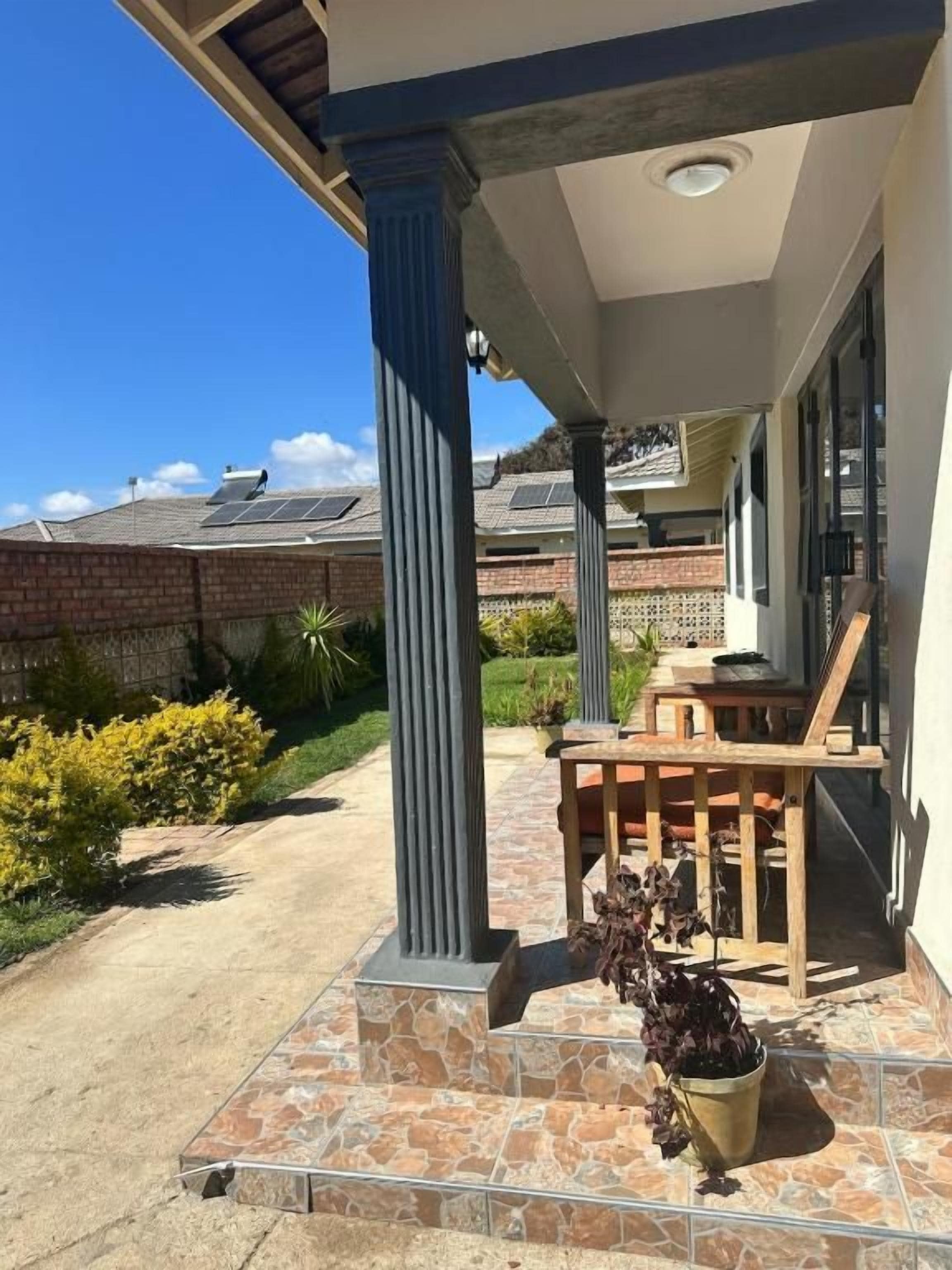 Un espace extérieur abrité, avec une table et des chaises de patio, une plante en pot et un mur de briques en arrière-plan.
