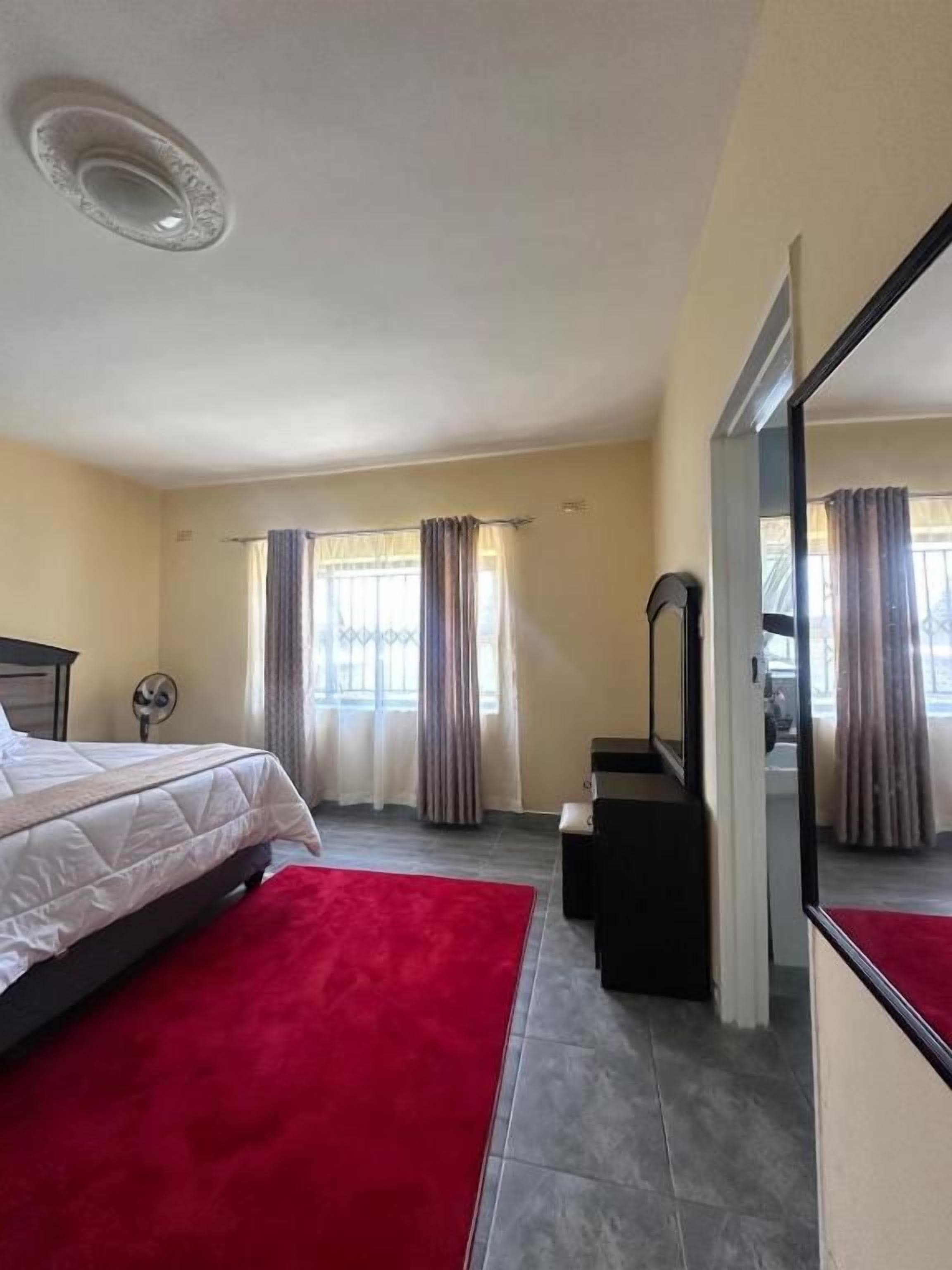 Una habitación de hotel con cama, alfombra roja, espejo y cortinas.