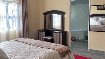 A bedroom with a bed, a desk, a mirror, and a bathroom visible through an open door.