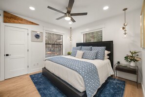 A bedroom with a bed, a ceiling fan, a nightstand, a lamp, and a window with blinds. - Sandbar Grand Estate, 4-Bedroom Luxury Retreat Near the University of Florida (Gainesville)