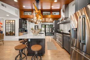 A modern kitchen with a central island, stainless steel appliances, and a wooden ceiling. - Sandbar Grand Estate, 4-Bedroom Luxury Retreat Near the University of Florida (Gainesville)