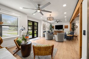 A modern living room with a ceiling fan, a flat-screen TV, and a dining area with a table and chairs. - Sandbar Grand Estate, 4-Bedroom Luxury Retreat Near the University of Florida (Gainesville)