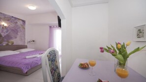 A hotel room with a bed, a dining table with a vase of flowers, and a breakfast setup. - Apartments Villa Angela - Studio Apartment With Terrace and Sea View (Baska Voda)