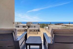 A balcony with two chairs and a table, overlooking a coastal view. - Marvelous Brand New 2 BR Condo - Pool With Ocean Views (Cabo San Lucas)