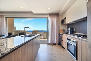 A modern kitchen with a central island, a microwave, a stove, and a view of the sea through the open door. - Marvelous Brand New 2 BR Condo - Pool With Ocean Views (Cabo San Lucas)