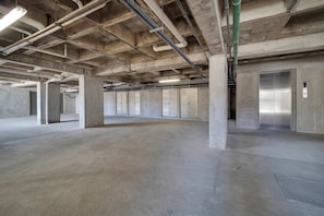 A spacious, unfinished parking garage with concrete pillars, exposed ceiling pipes, and a metallic elevator. - Marvelous Brand New 2 BR Condo - Pool With Ocean Views (Cabo San Lucas)