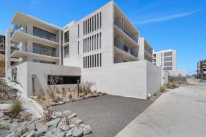 A modern multi-story building with balconies, a landscaped area with rocks and cacti, and a clear sky. - Marvelous Brand New 2 BR Condo - Pool With Ocean Views (Cabo San Lucas)
