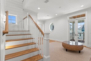 A staircase with wooden steps and white railings, a round woven coffee table, and a large window with a view of the outside. - Stunning 6 Bedroom Sugar Sands Home, Private Pool, Sleeps 14 (Mexico Beach)