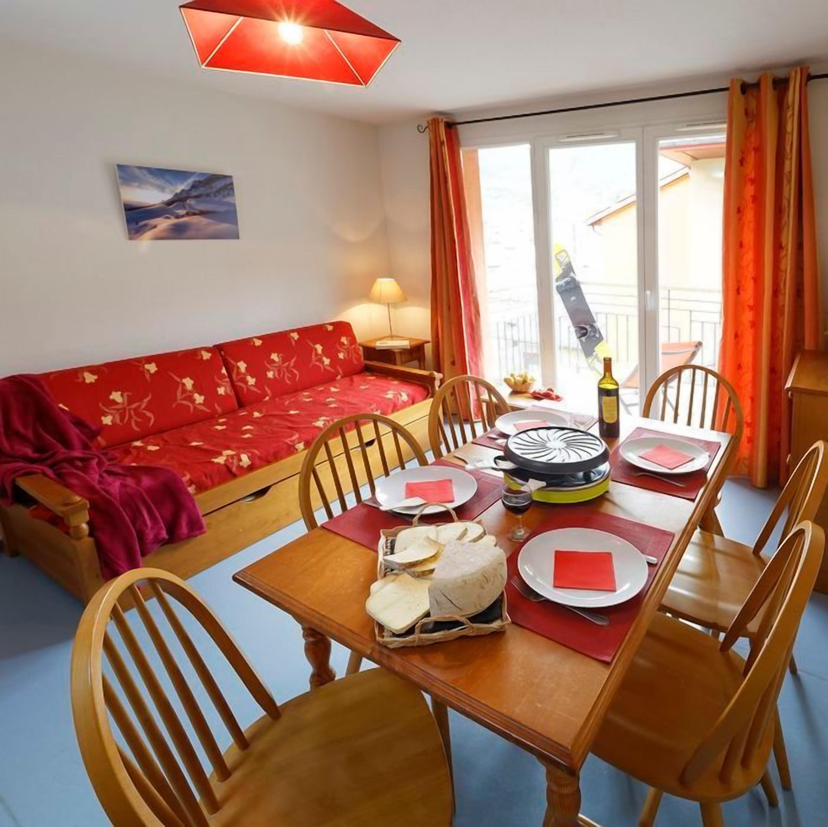 Un coin repas avec une table dressée pour quatre personnes, un canapé rouge et un balcon avec vue.