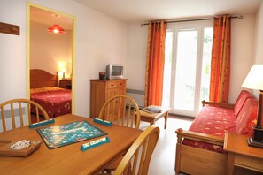 A room with a bed, a desk with a computer, a chair, a table with a board game, and a window with curtains. - Ski aux pieds | Piscine chauffee sur place (Ax-les-Thermes)