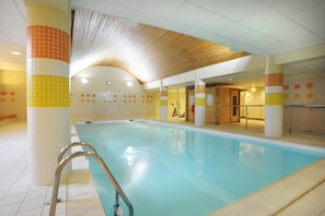 An indoor swimming pool with a tiled floor, a metal ladder, and a wooden ceiling. - Ski aux pieds | Piscine chauffee sur place (Ax-les-Thermes)