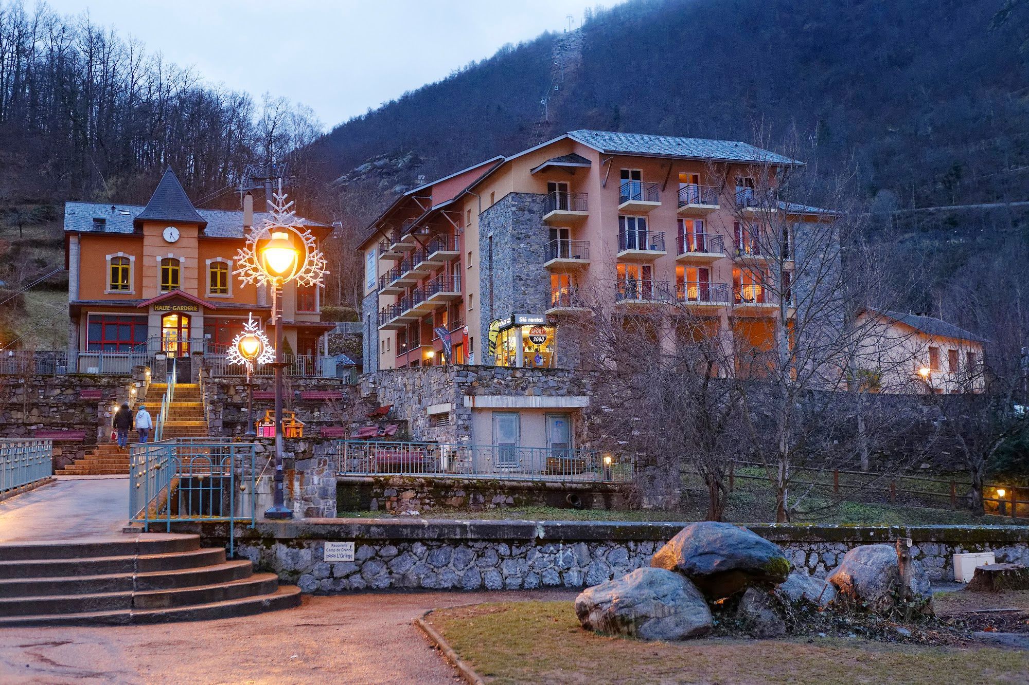 A multi-story hotel with a stone facade, a ski rental sign, and a well-lit entrance.