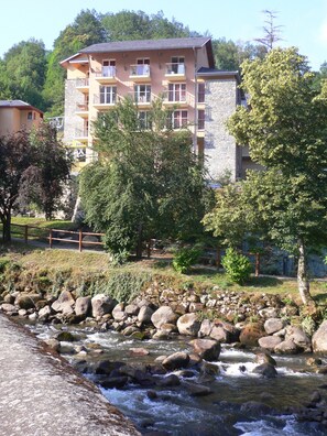 Un immeuble à plusieurs étages doté de balcons, d’une façade en pierre et avec une rivière en premier plan.
