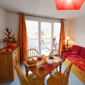 Ein Essbereich mit einem Tisch für zwei Personen, einem roten Sofa und Blick auf die Stadt durch große Fenster.
