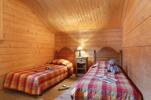 Une chambre dans un chalet en bois, avec deux lits, une table de chevet, une lampe et un ours en peluche.