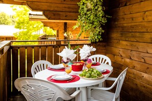 A wooden deck with a table set for a meal, surrounded by chairs. - Balcon vue montagne | Piscine chauffée | Sauna (Morillon)