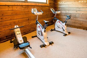Deux vélos d’appartement équipés d’écrans numériques, placés dans une pièce aux murs en bois et au sol recouvert de moquette.