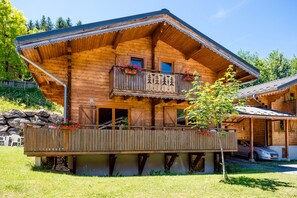 Un chalet en bois doté d’un balcon, d’une véranda et d’un mur de pierre en arrière-plan.