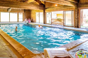 An indoor swimming pool with wooden walls and a view of the outside. - Balcon vue montagne | Piscine chauffée | Sauna (Morillon)