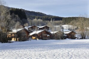 A row of wooden cabins with snow-covered roofs, surrounded by a forested mountain backdrop. - Balcon vue montagne | Piscine chauffée | Sauna (Morillon)