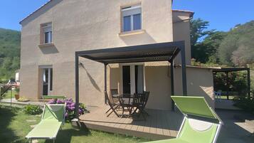 A two-story house with a patio area, a covered seating area, and a small garden.