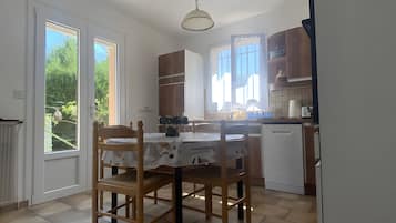 A kitchen with a dining table, chairs, a refrigerator, and a window with curtains.